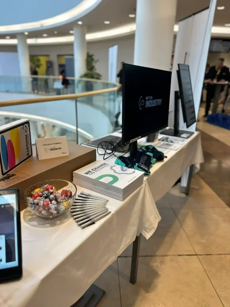 Stánek Better Industry s monitorem, propagačními materiály a cukrovinkami na konferenci.