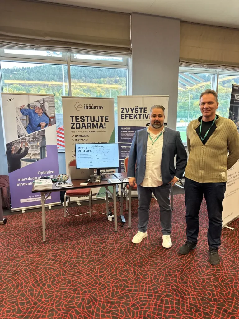 Dva členové týmu Better Industry stojí před prezentačním stánkem s roll‑upy a ukázkou softwaru na konferenci.