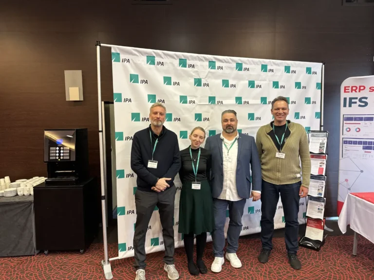 Skupinová fotografie účastníků konference IPA před oficiální fotostěnou s logem IPA, s přístupovými kartami na krku.